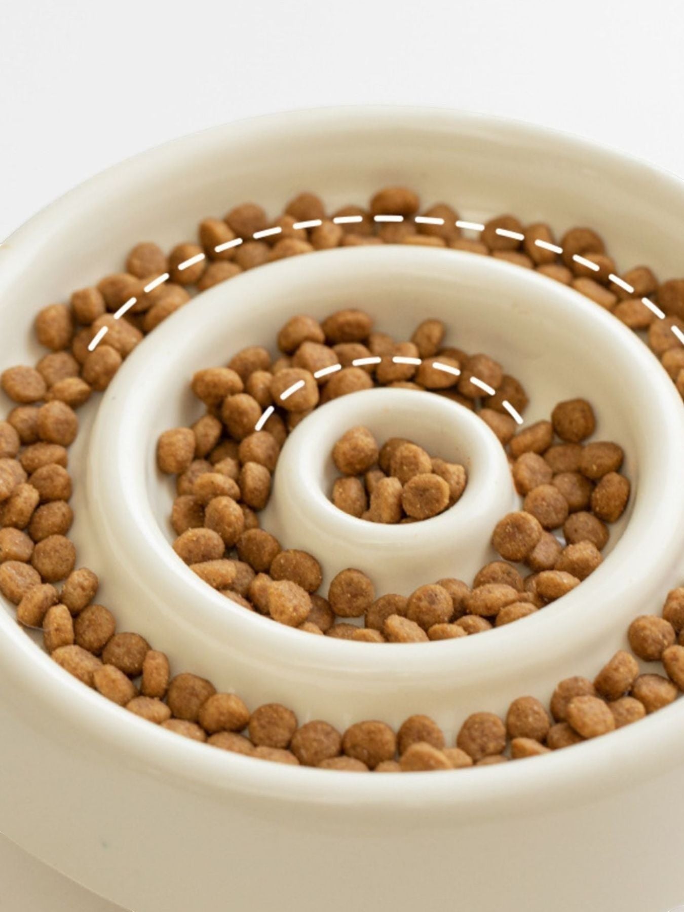 Little Pets Club cream ceramic slow feeder dog and cat bowl with spiral pattern filled with kibble.