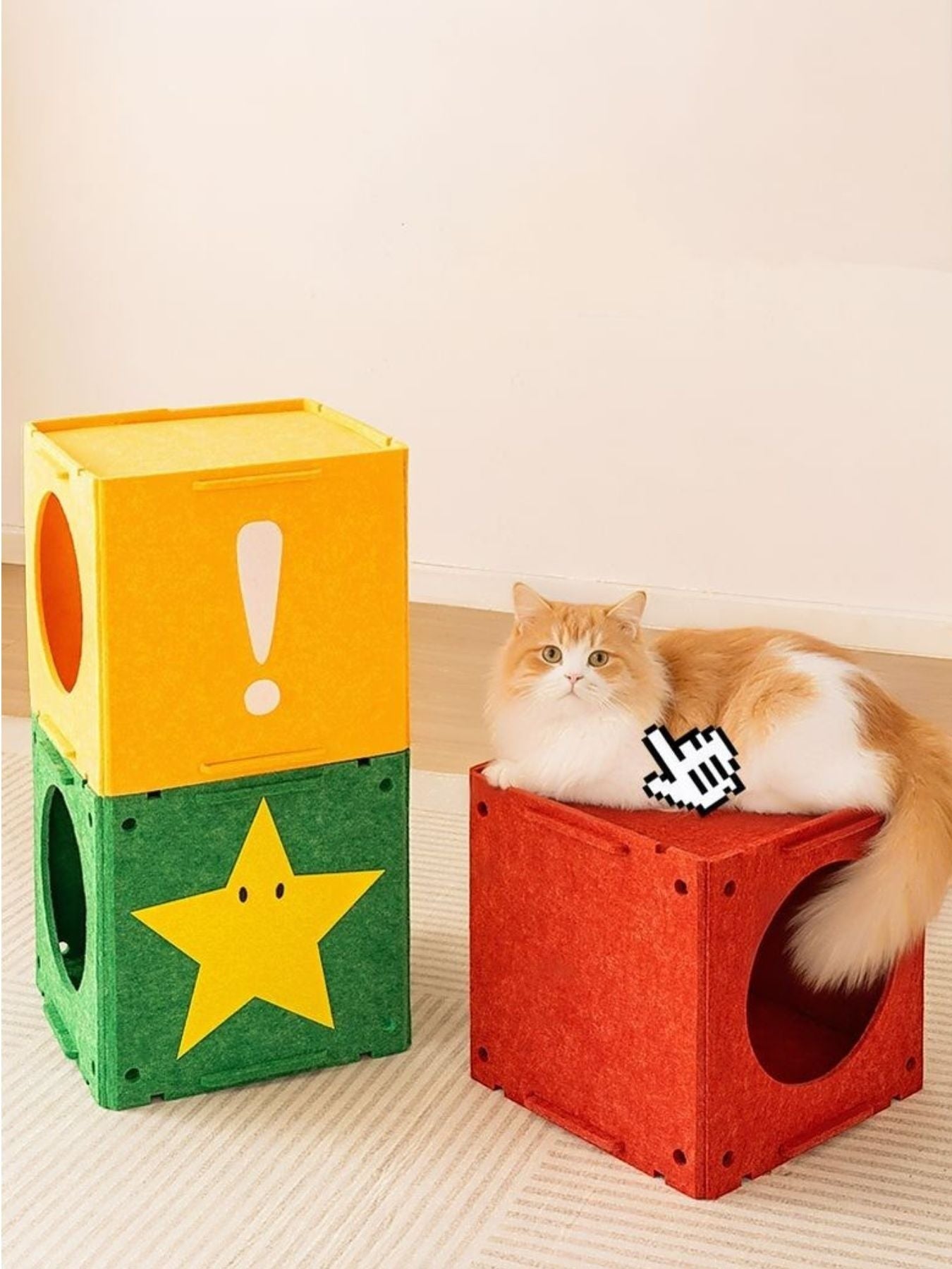 Orange and white cat lounging on a red felt cube next to a stack of green and yellow felt cat cubes with cutouts and game-inspired graphics.