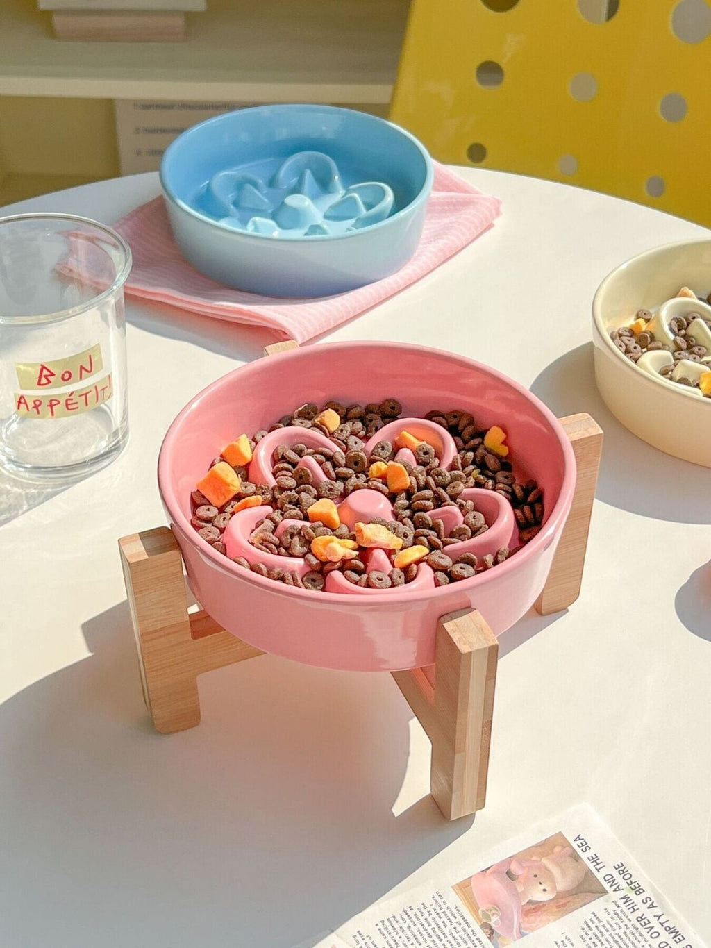 Little Pets Club pink ceramic flower slow feeder pet bowl with wooden stand, filled with kibble and treats.