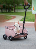 Little Pets Club pink portable pet stroller wagon with a small white dog inside, being pushed by a person outdoors.