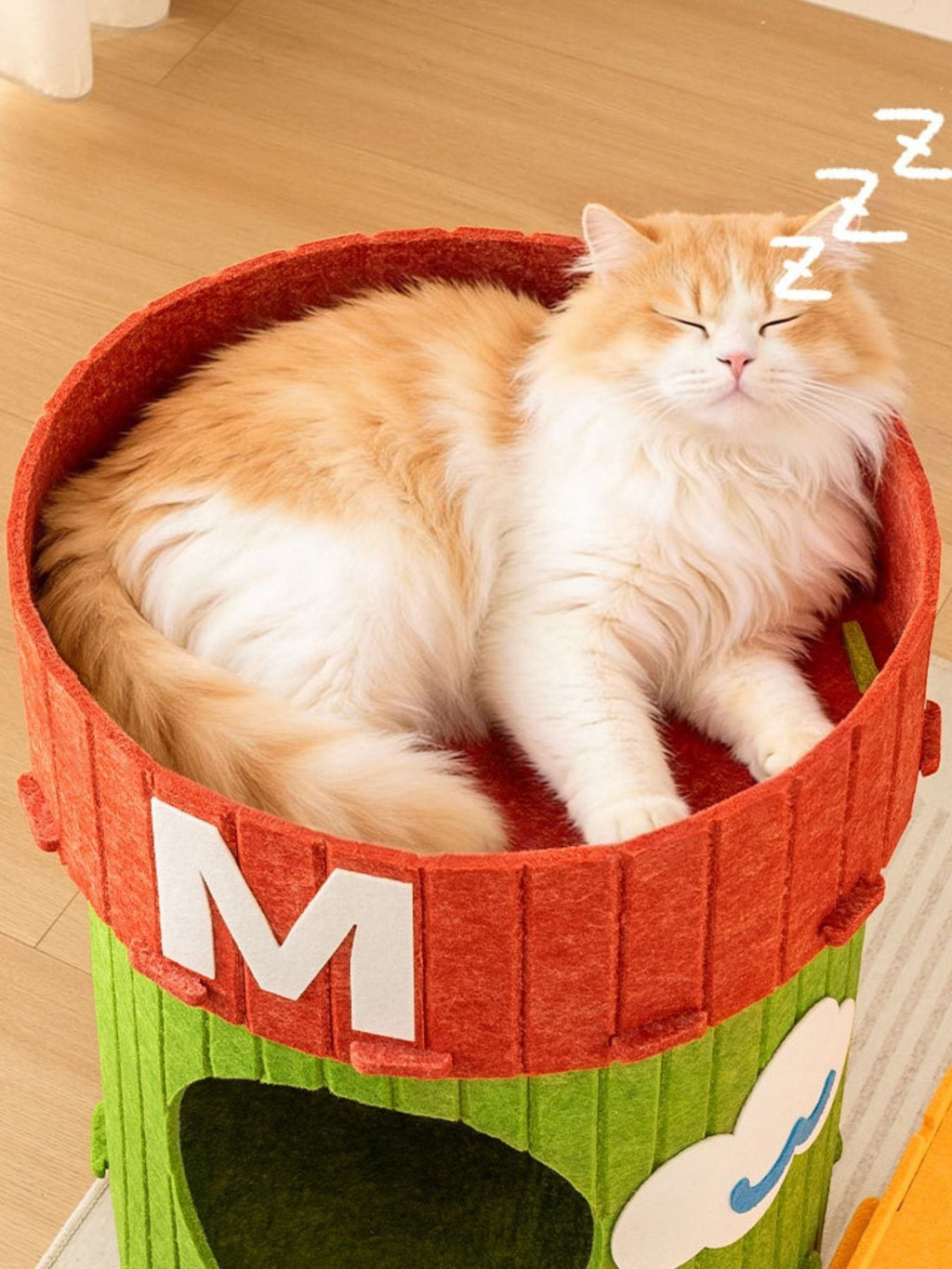 Orange and white cat sleeping in a green and red felt cat house with a cloud design.